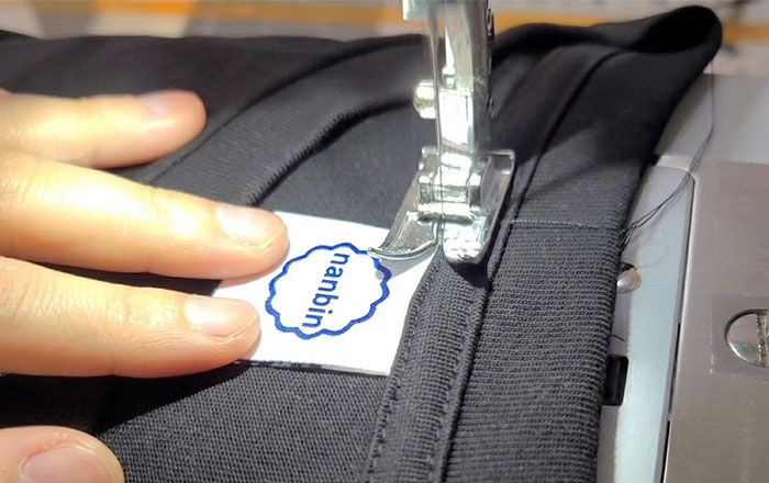 Factory worker sewing a Nanbin brand label onto black shapewear for private label manufacturing